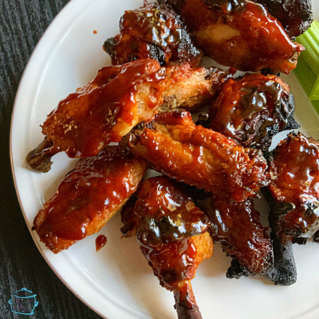 looking down on a plate of crispy, saucy wings with celery on the side