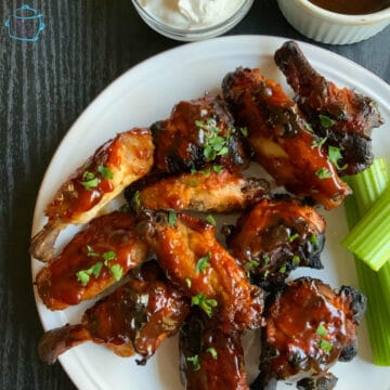 looking down on a plate of crispy, saucy wings with celery on the side
