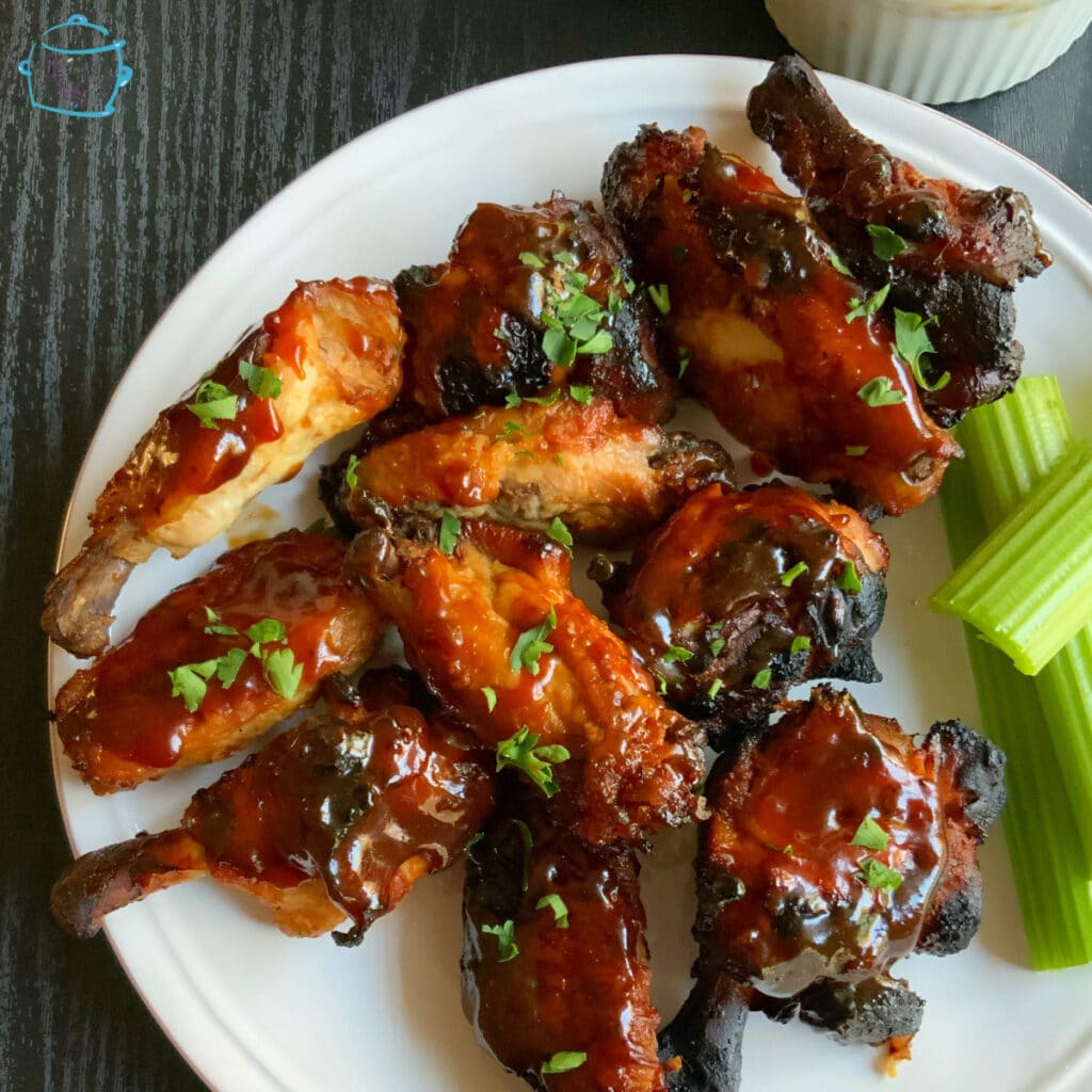 looking down on a plate of crispy, saucy wings with celery on the side