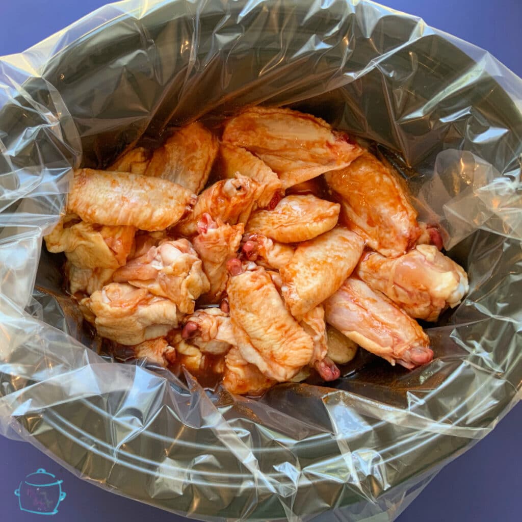 a crockpot with a liner filled with wings and sauce