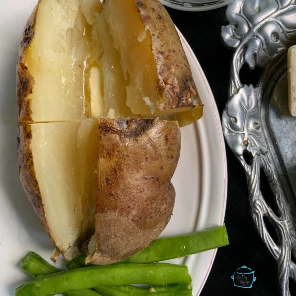 Close up of an baked potato cut open with butter and some green beans off to the side