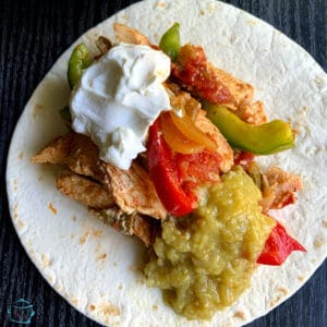 Chicken, peppers, sour cream and guacamole laying on top of a flour tortilla
