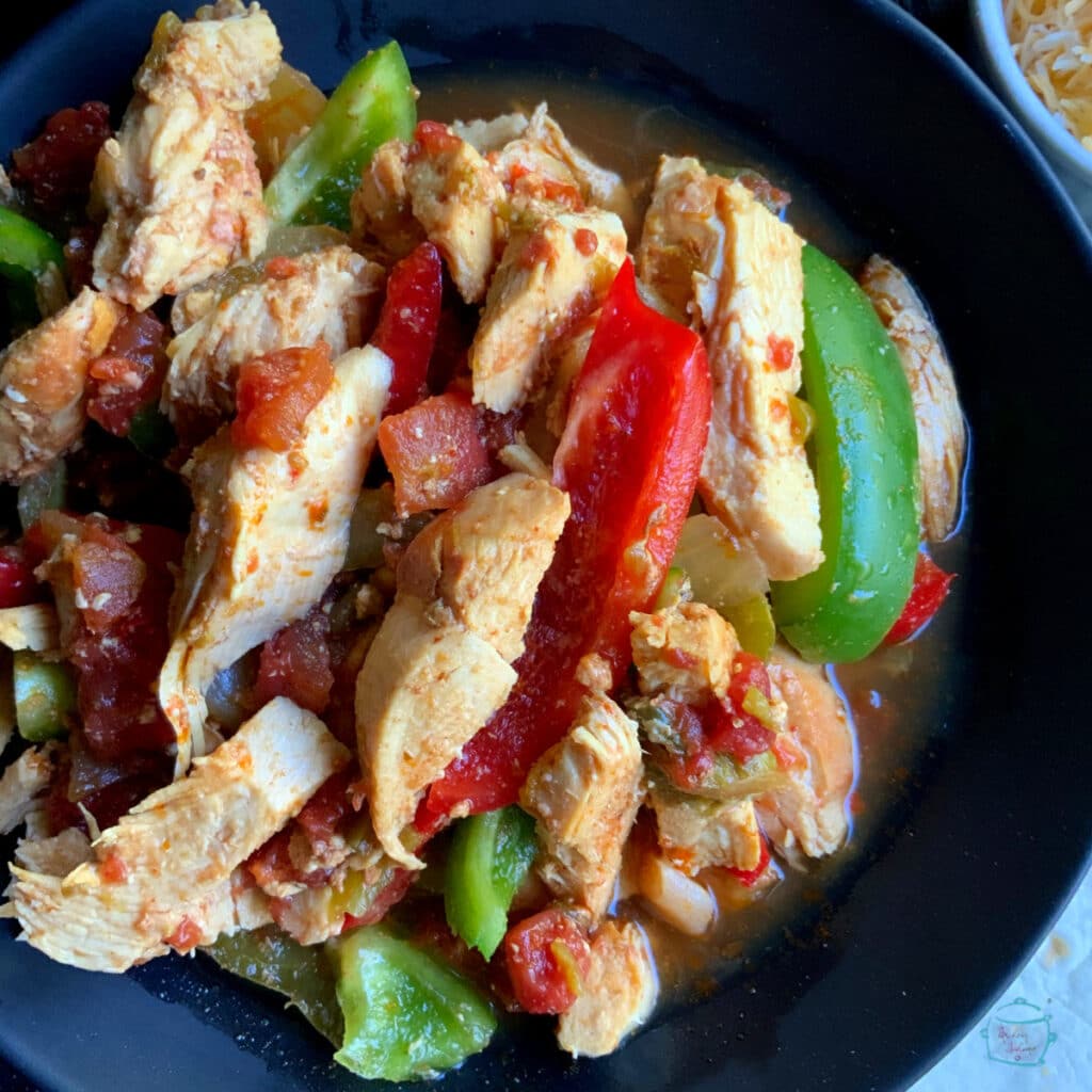 Cooked chicken, peppers and onions in a black bowl