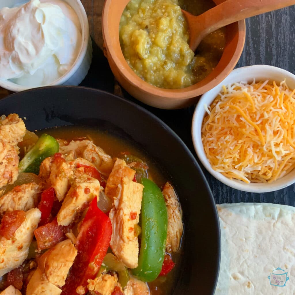 A bowl of chicken and peppers next to smaller bowls with toppings