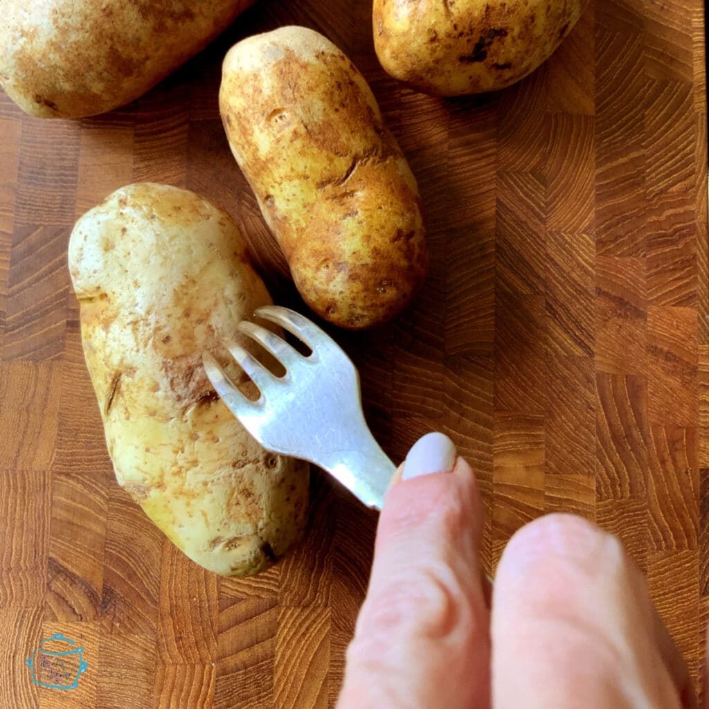 Potatoes laying on a wooden board, one is being poked with a fork