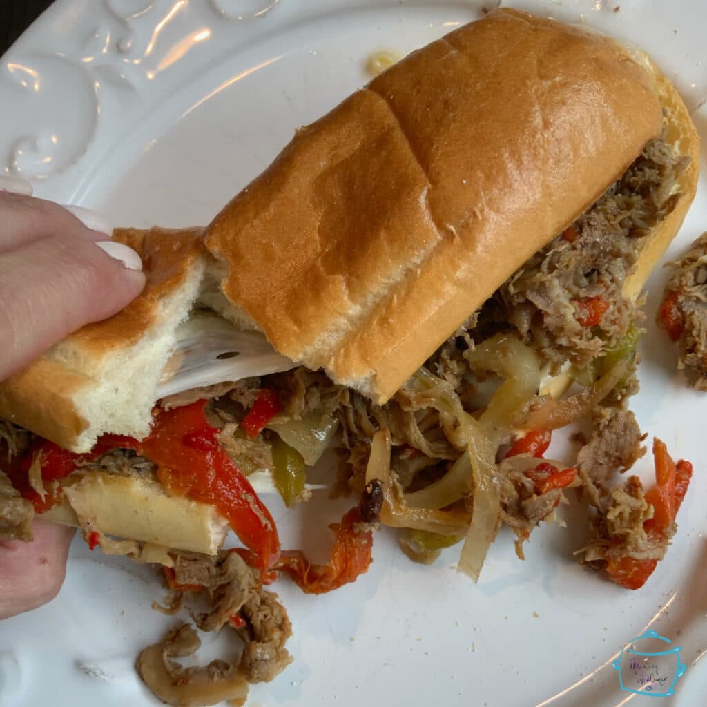 Two hands pulling different sides of a cut sandwich with cheese stretching between the halves