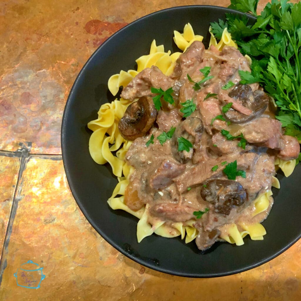 Plated beef stroganoff on noodles with some greens off to the side