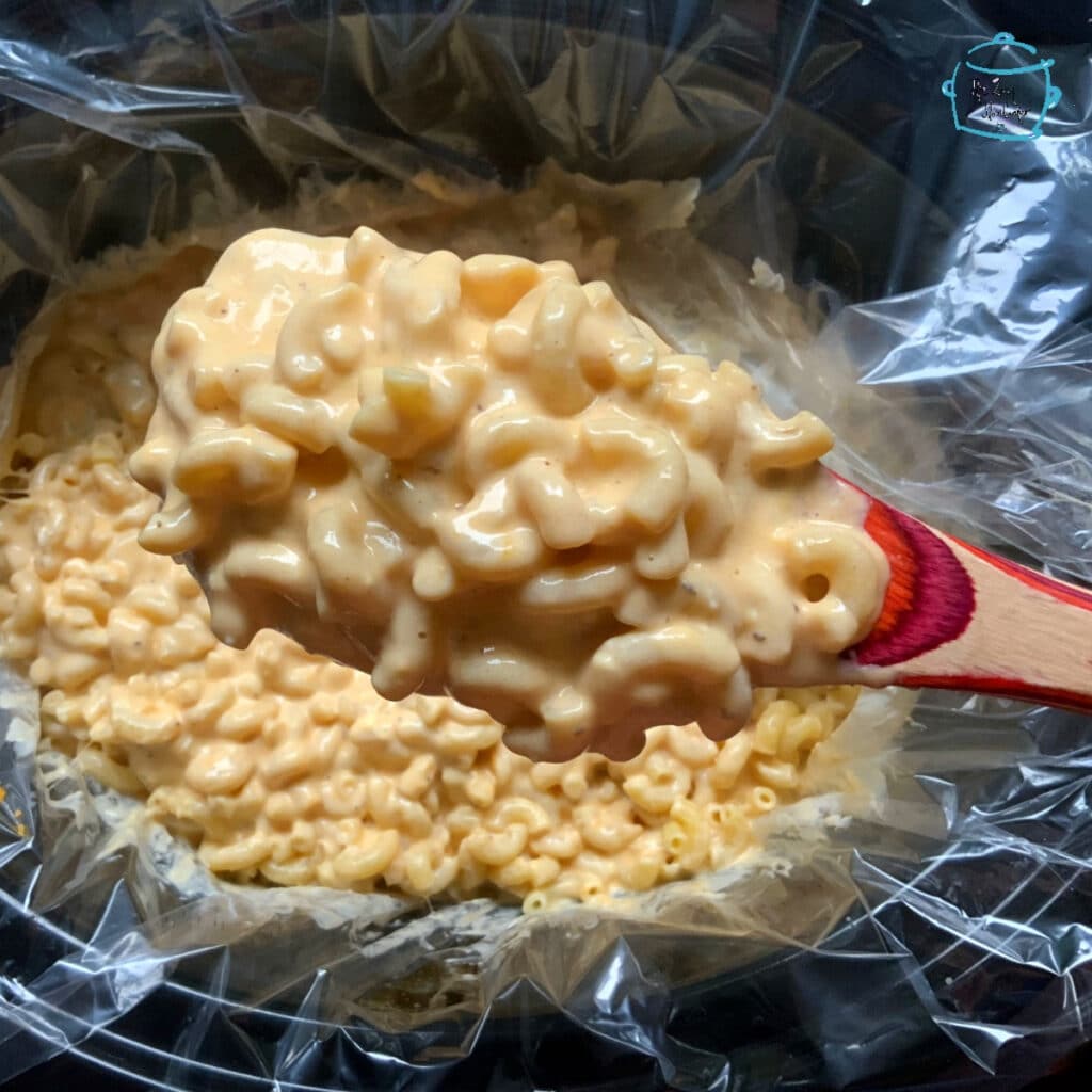 Large spoonful of slow cooker old bay mac and cheese held over a full crockpot of the same 