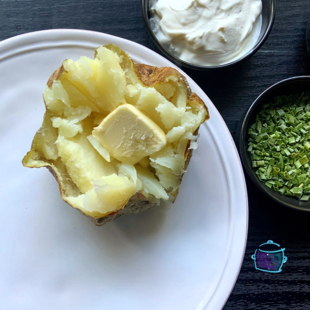 an open potato on a white plate with a pat of butter in the middle