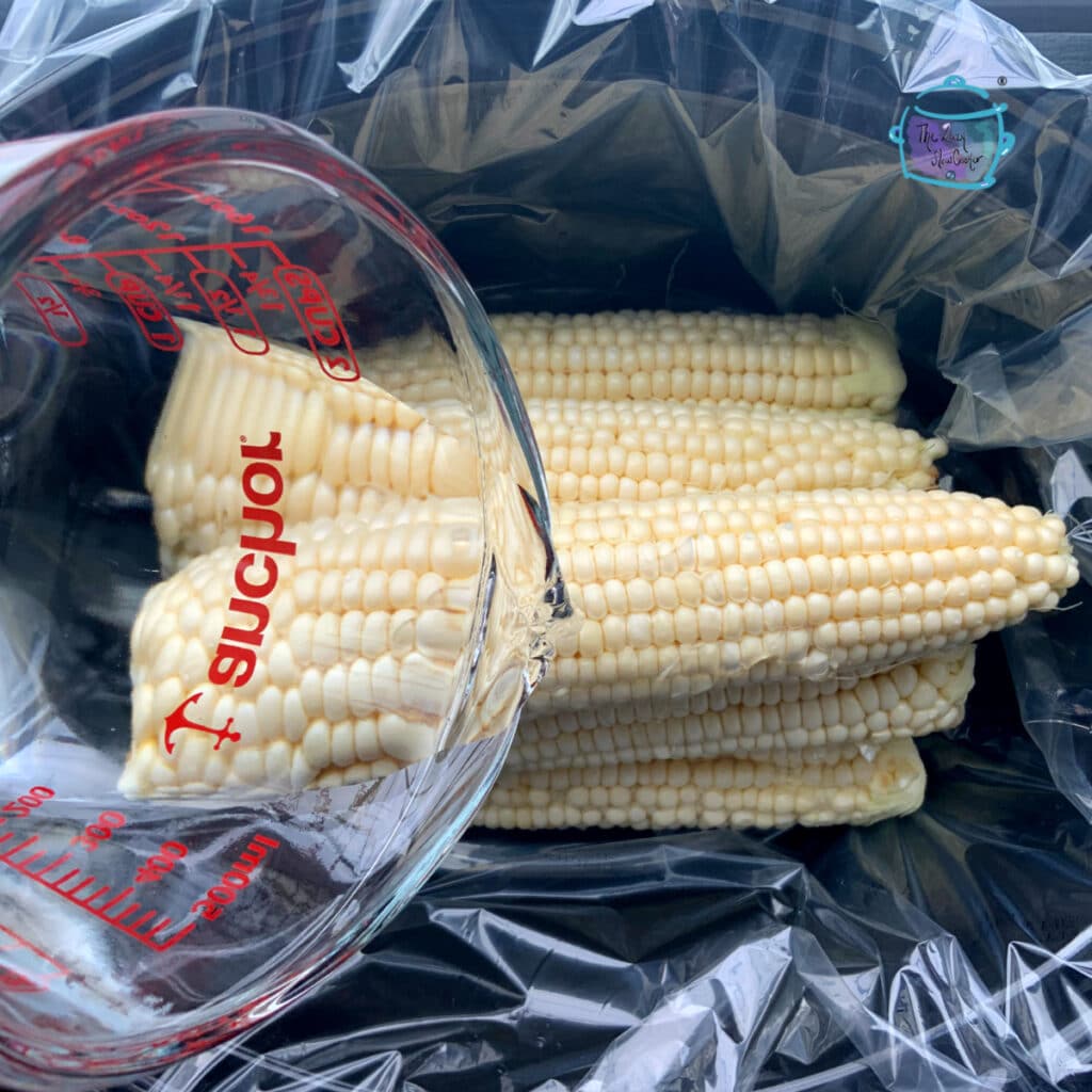 multiple ears of corn in slow cooker with water being added