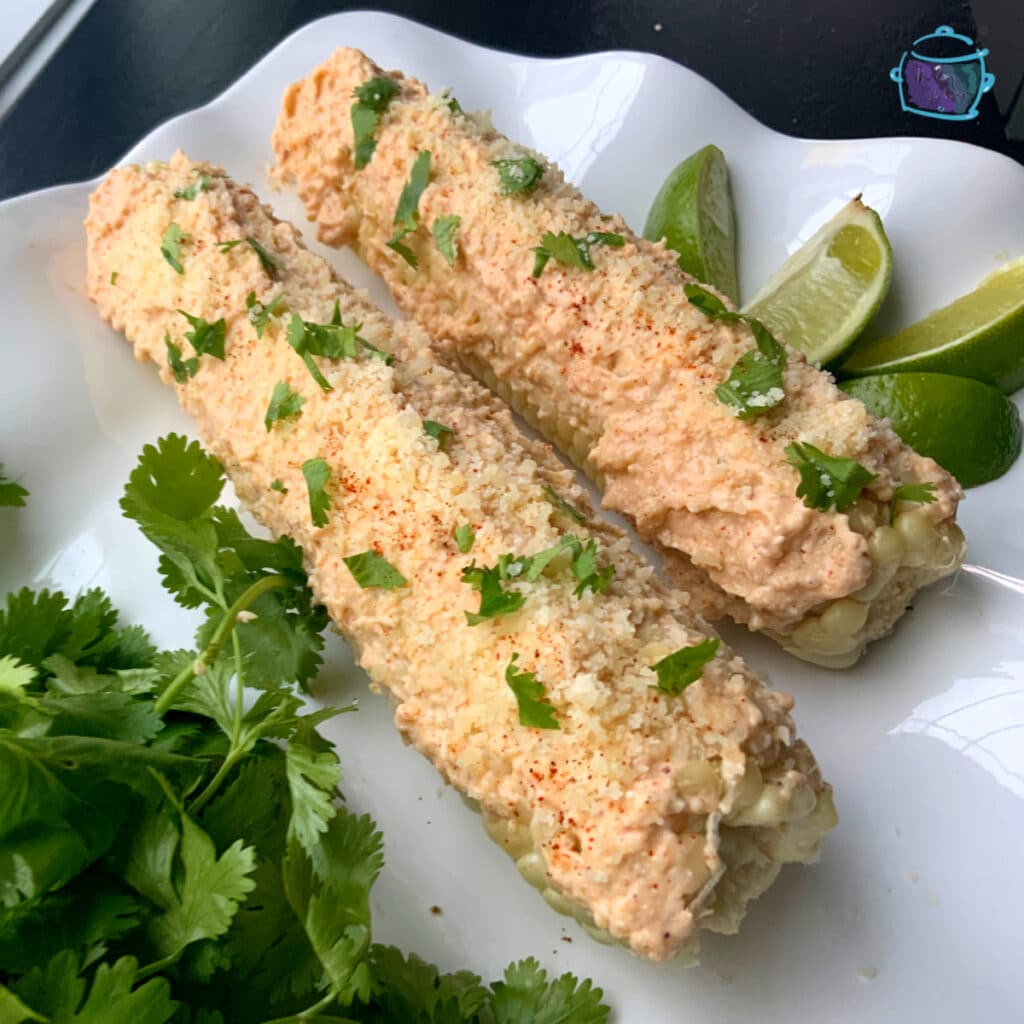 two elote on a white tray with lime wedges and cilantro