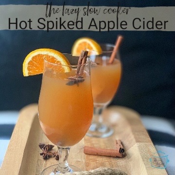two glassed filled with a hot spiked apple cider garnished with an orange slice and cinnamon stick