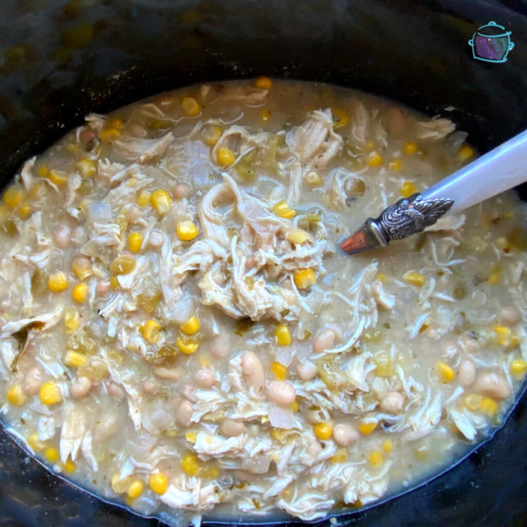 An oval slow cooker filled with chicken chili and a white spoon