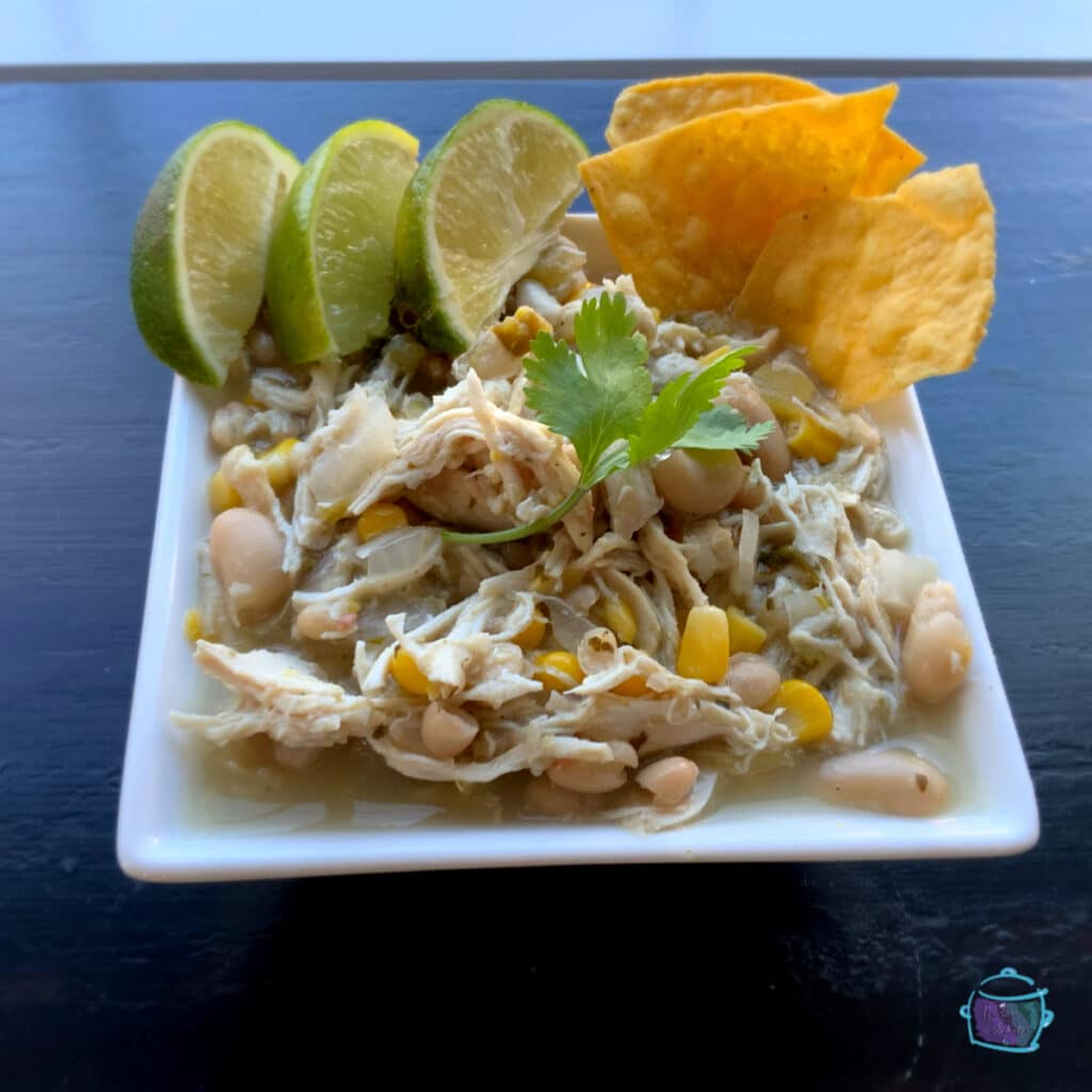 A side view of chicken chili with fresh cilantro, lime and chip on the side