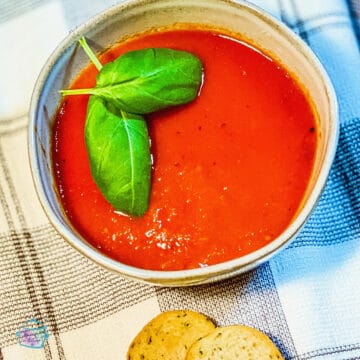 A bowl of tomato soup with basil leaves on top