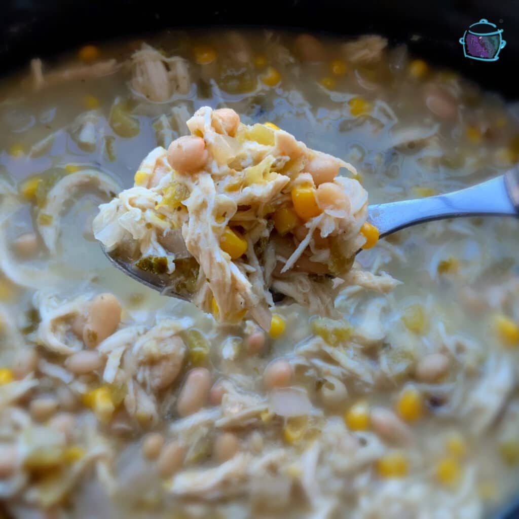 White chicken chili on a spoon held close to the camera with a post of the same in the background