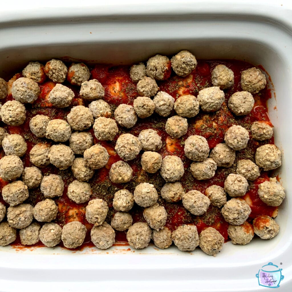 A rectangular slow cooker showing the meatball layer on top of a layer of sauce