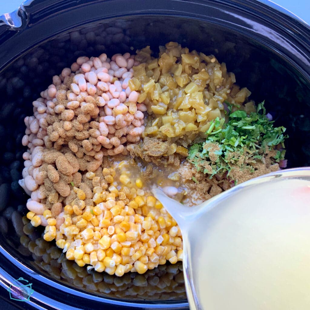 All ingredients in slow cooker with chicken stock being poured on top