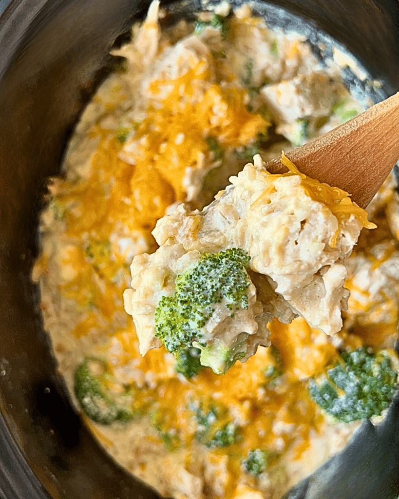 Cooked chicken broccoli and rice in crockpot with a wooden spoon