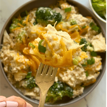 a bowl filled with slow cooker chicken broccoli and rice with a mouthful on a fork