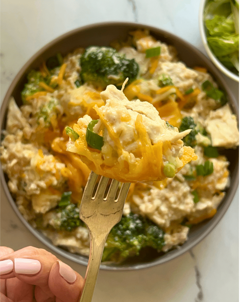 a bowl filled with slow cooker chicken broccoli and rice with a mouthful on a fork