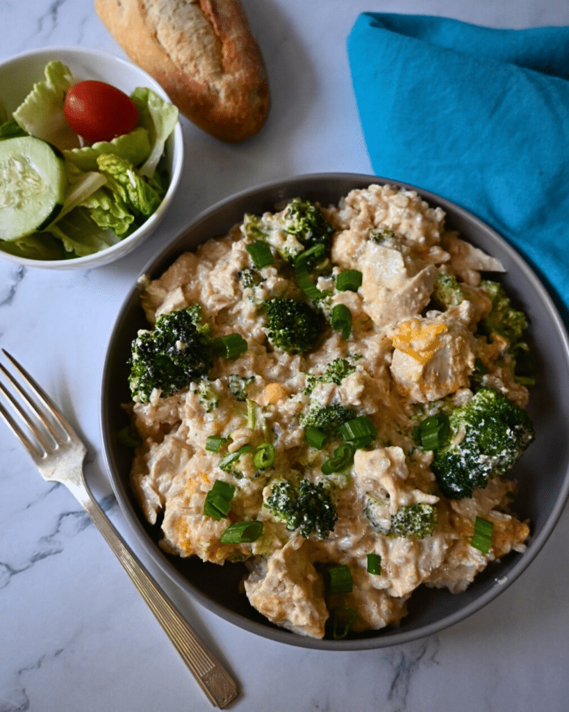 a bowl filled with slow cooker chicken broccoli and rice with a fork and salad on the side.