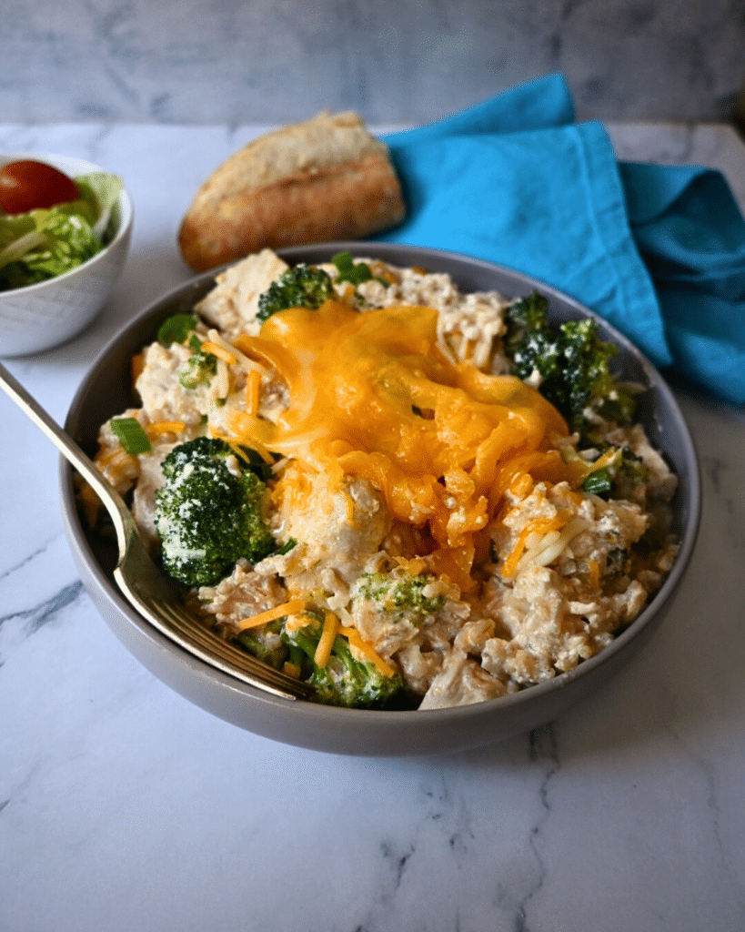 a bowl filled with slow cooker chicken broccoli and rice with a fork and salad on the side.