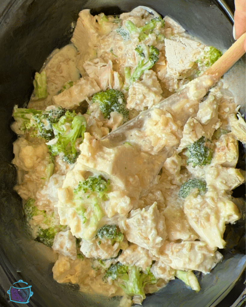 Cooked chicken broccoli and rice in crockpot with a wooden spoon