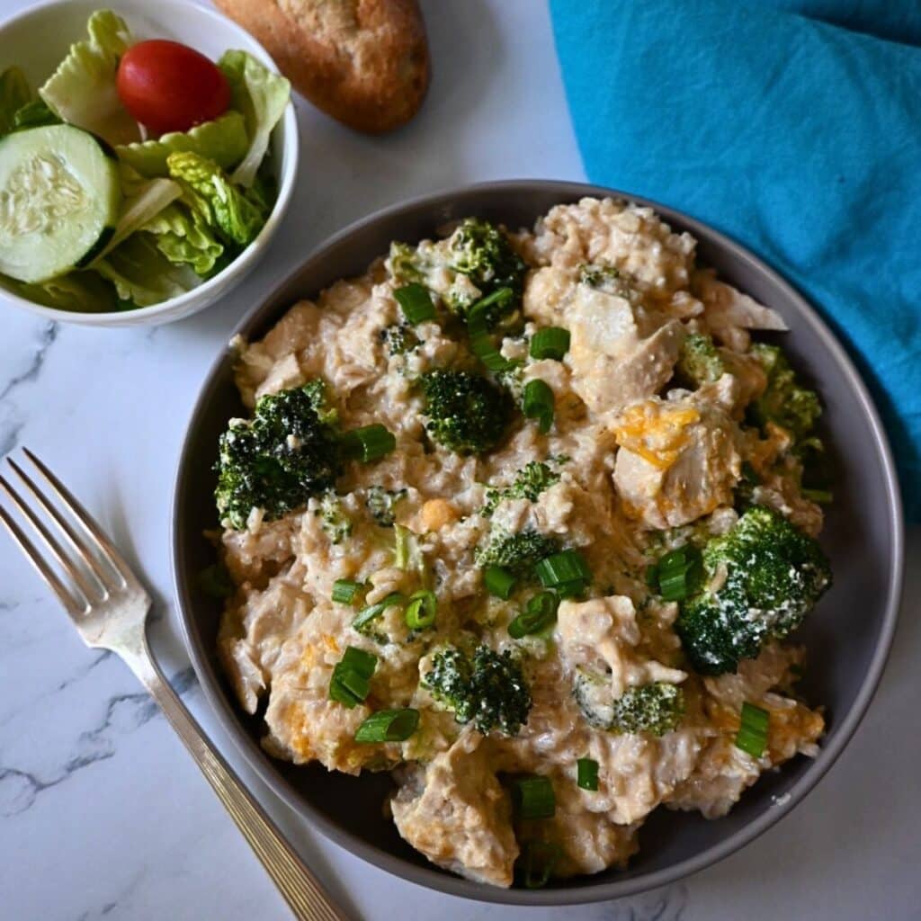 a bowl filled with slow cooker chicken broccoli and rice with a fork and salad on the side.