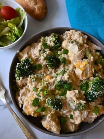a bowl filled with slow cooker chicken broccoli and rice with a fork and salad on the side.