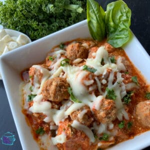 A square bowl filled with meatballs and melted cheese with basil