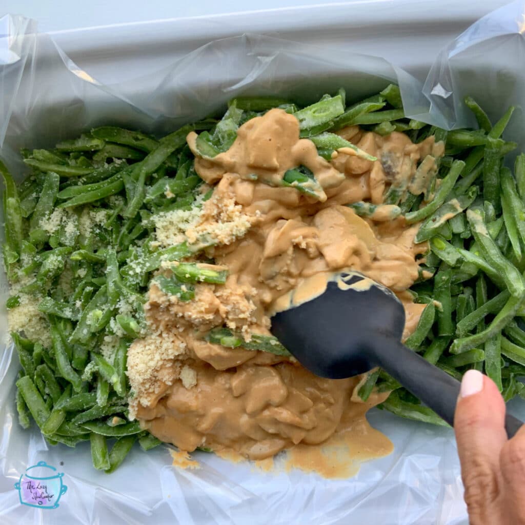 Green beans in a rectangular slow cooker being stirred together with sauce and mushoromos