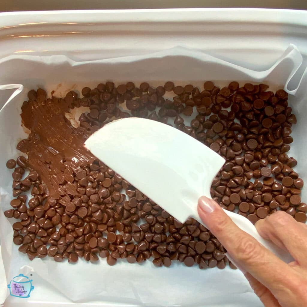 Melted chocolate chips in a slow cooker being smoothed out into a single layer with a spatual