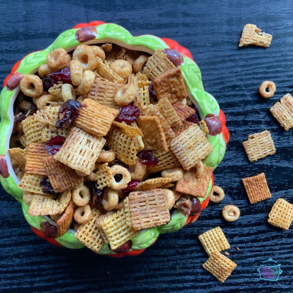 A round orange and green bowl holding pumpkin pie snack mix