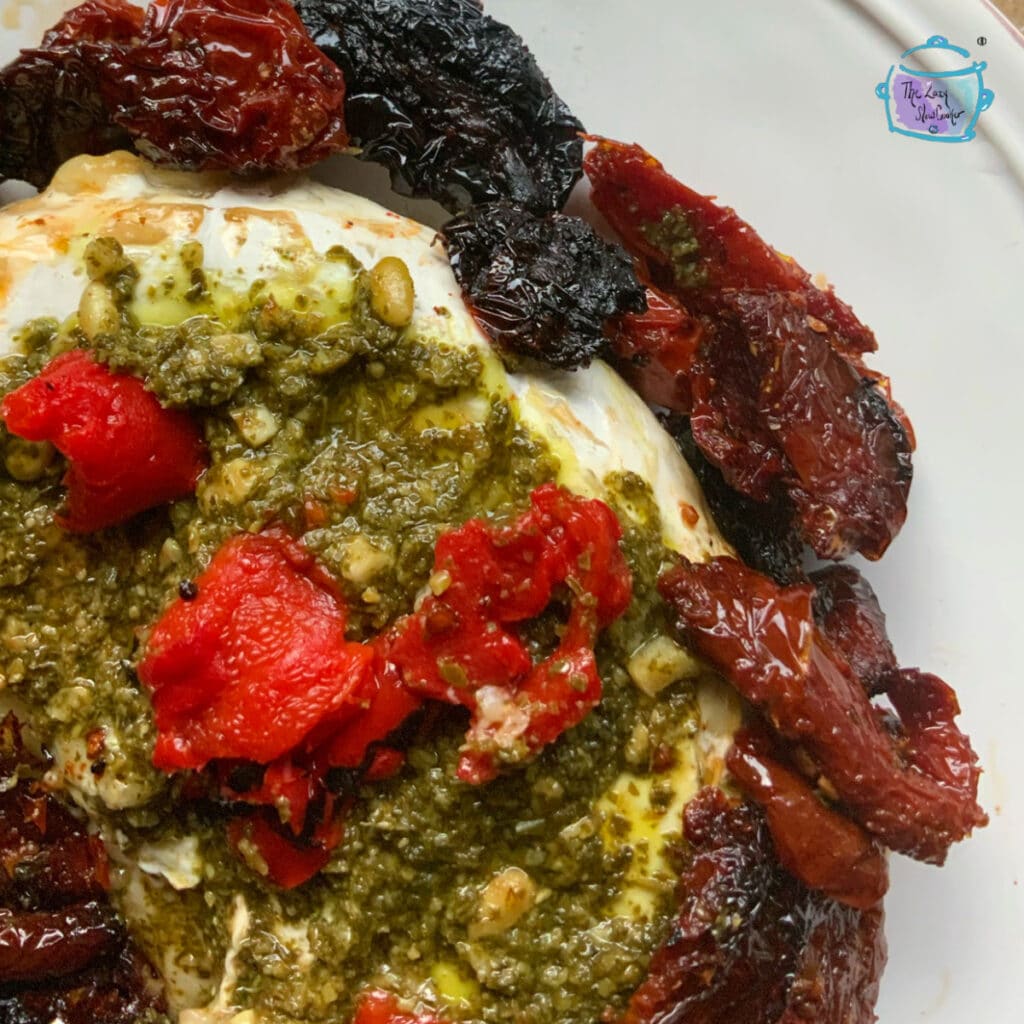 close up of slow cooker brie topeed with pesto, sun dried tomatoes and roasted red peppers