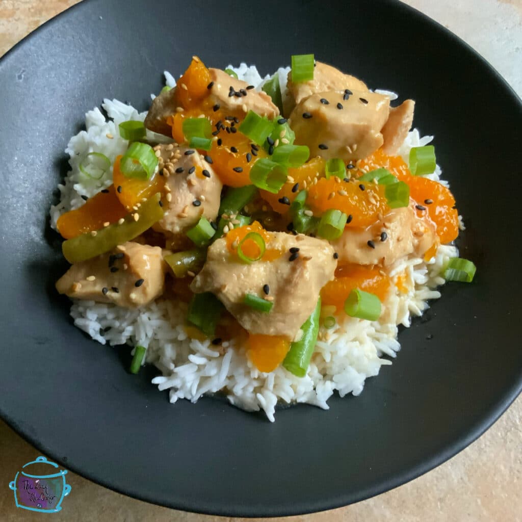 Mandarin orange slow cooker chicken over rice on a rotund black plate