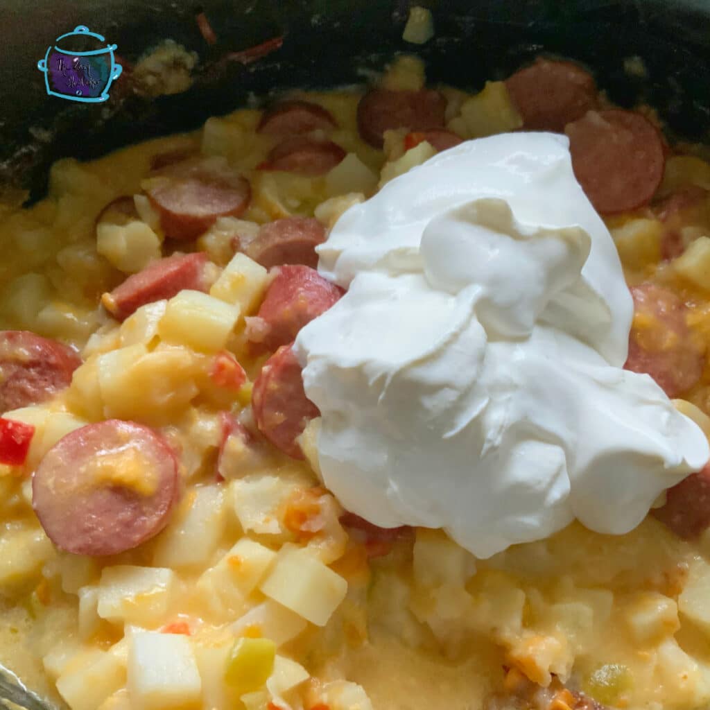 Cheesy potatoes and kielbasa in slow cooker with a sour cream laying on top