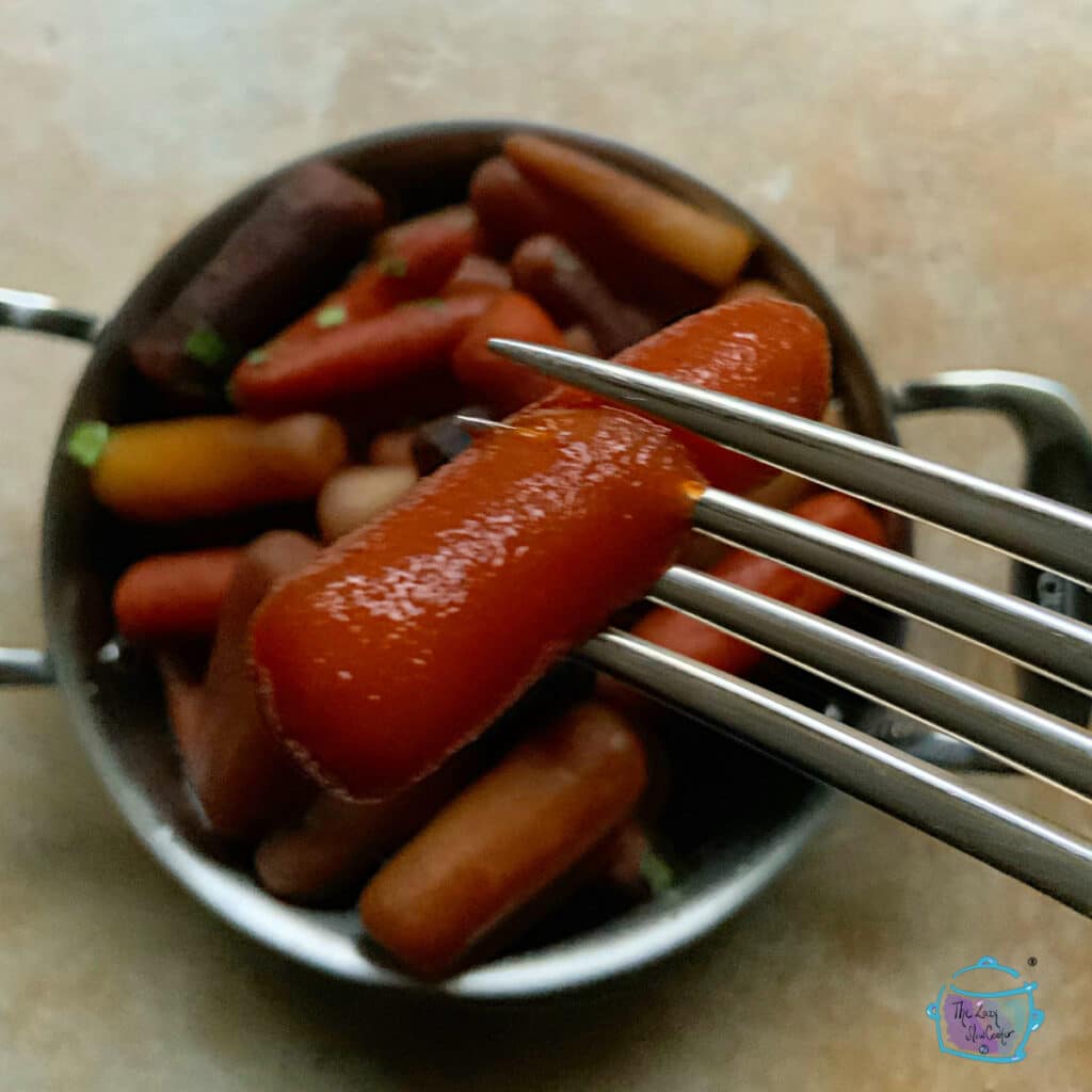 One cooked carrot on a fork held closer to the camera with some blurred carrots in the background