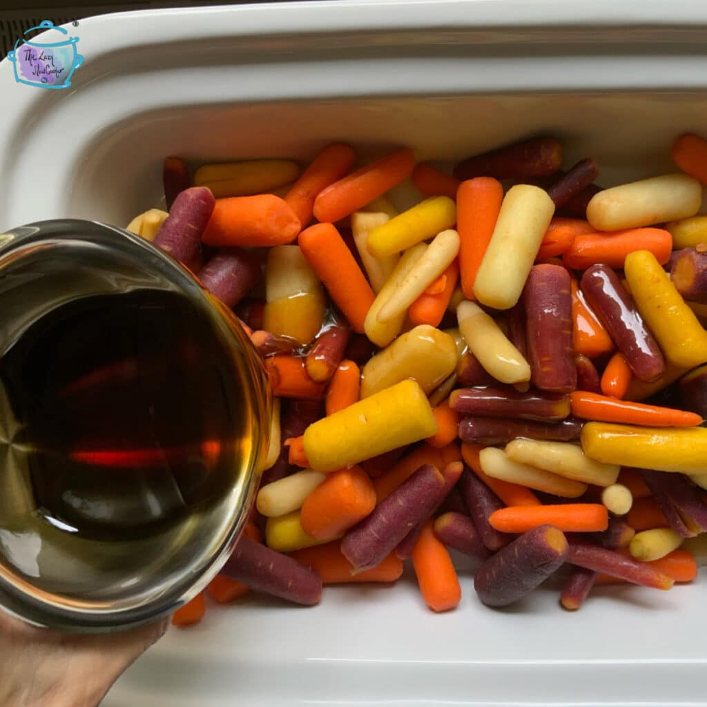 raw carrots in slow cooker with other ingredients being poured overtop