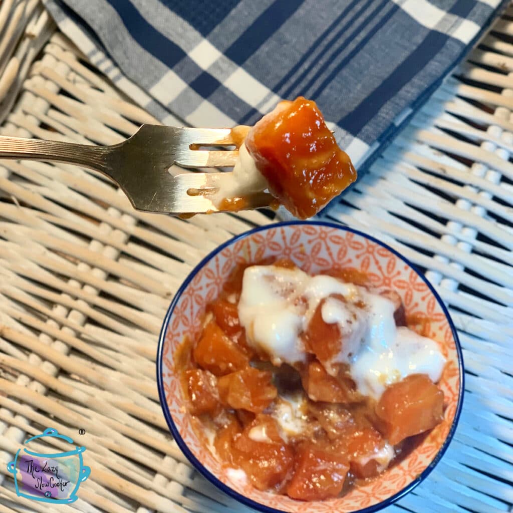 A bowl of finished slow cooker candied sweet potatoes with one being held on a fork close to the camera