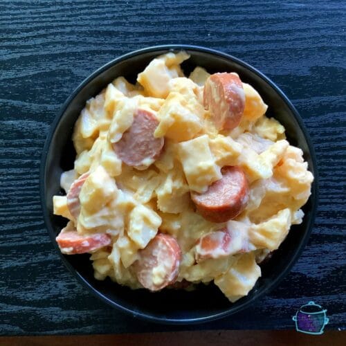 a black round bowl filled with a cheesy combo of kielbasa and potatoes
