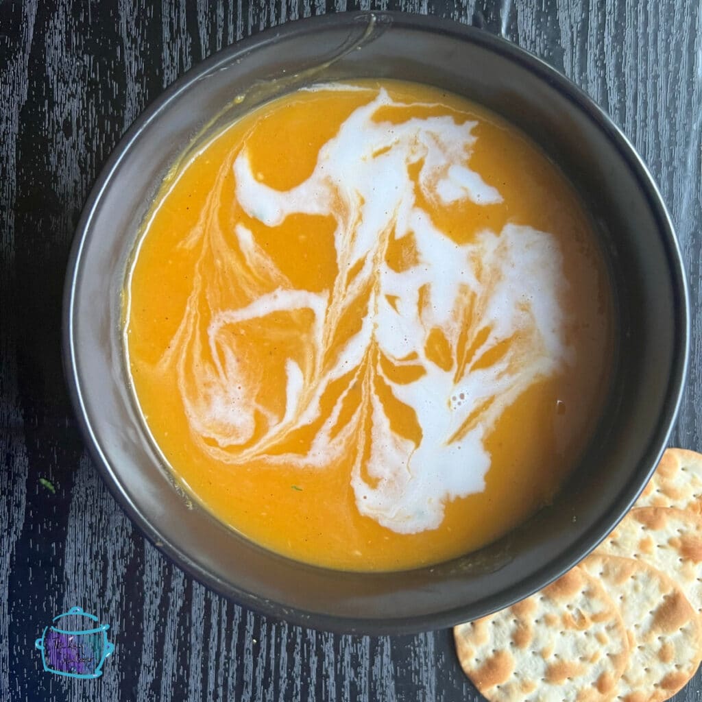 A bowl of butternut squash soup ready to serve with crackers on the side