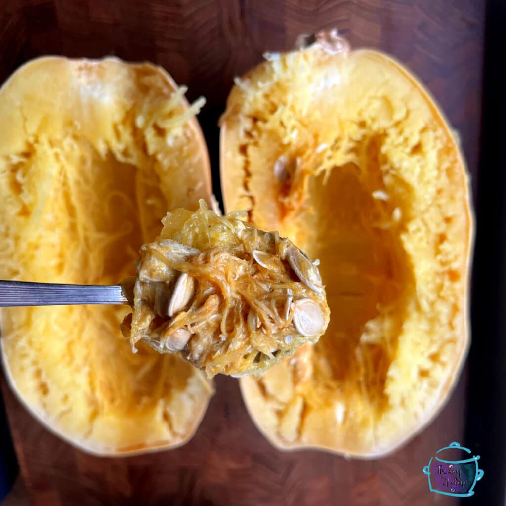 Spaghetti squash cut in half with a spoon holding seeds and pulp