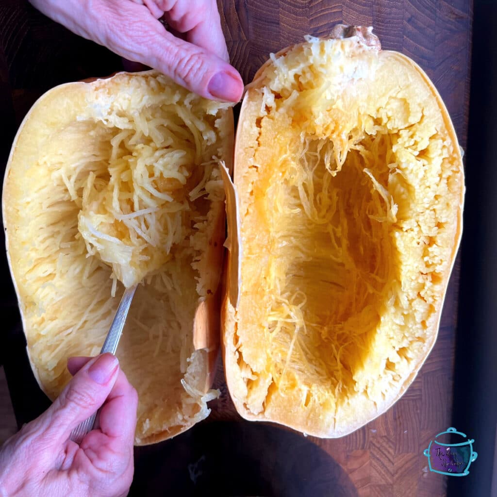 An open spaghetti squash with a utensil demonstrating how to pull into spaghetti-like strands