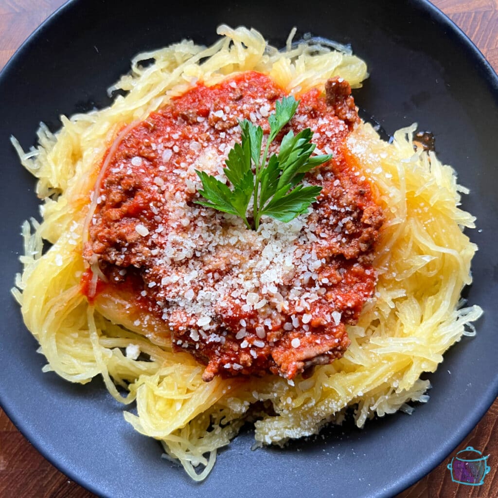 Spaghetti squash on a plate topped with meat sauce and some fresh herbs