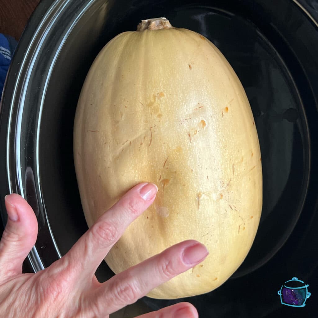 whole squash in crockpot after cooking with a finger making a dent showing it is finished