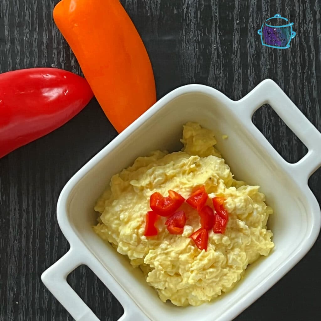 crockpot egg salad in a white bowl topped with some chopped red peppers