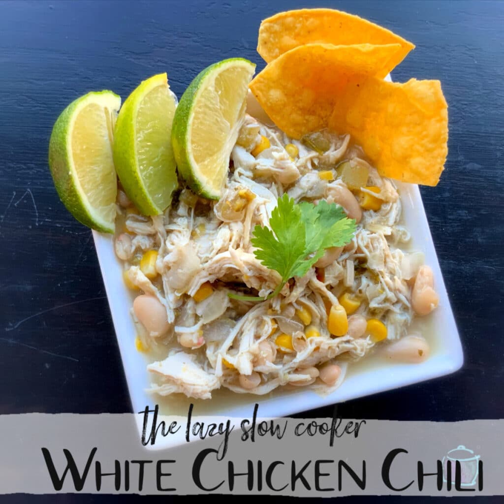 a bowl of white chicken chili with some lime slices and tortilla chips on the side