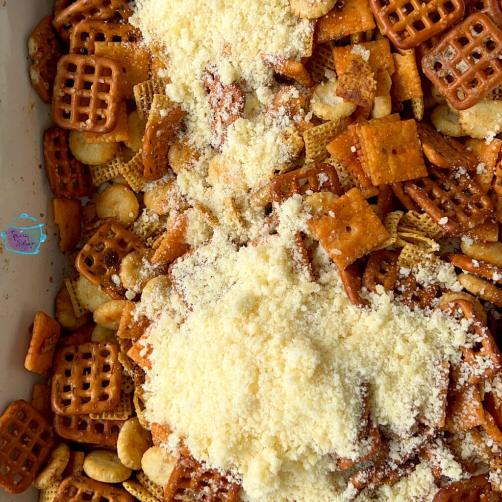 Snack mix in slow cooker with parmesan cheese on top before mixing