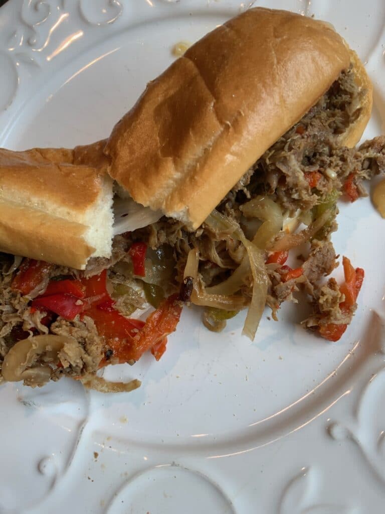 A cheesesteak sandwich laying on a plate that has been ripped in half